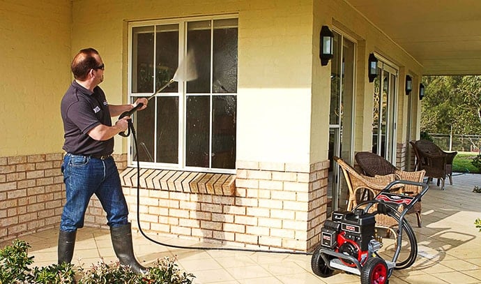 A man cleaning a house with a pressure washer.